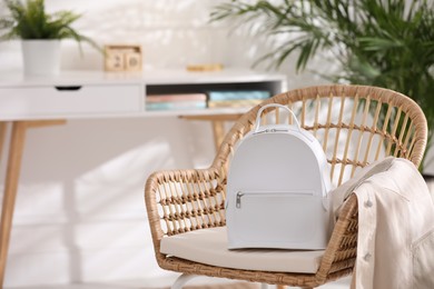 Photo of Stylish white backpack and jacket on wicker chair indoors, space for text