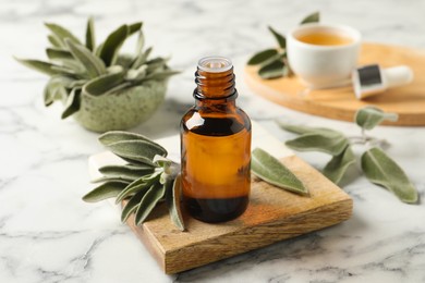 Photo of Bottle of essential sage oil and leaves on white marble table