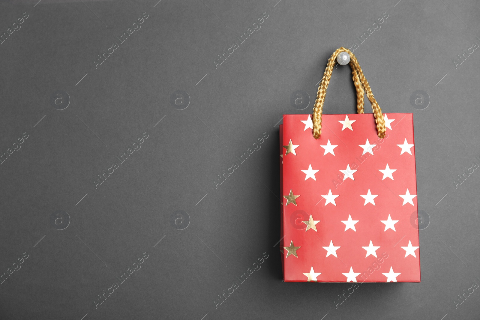 Photo of Red shopping paper bag with star pattern on black background, space for text