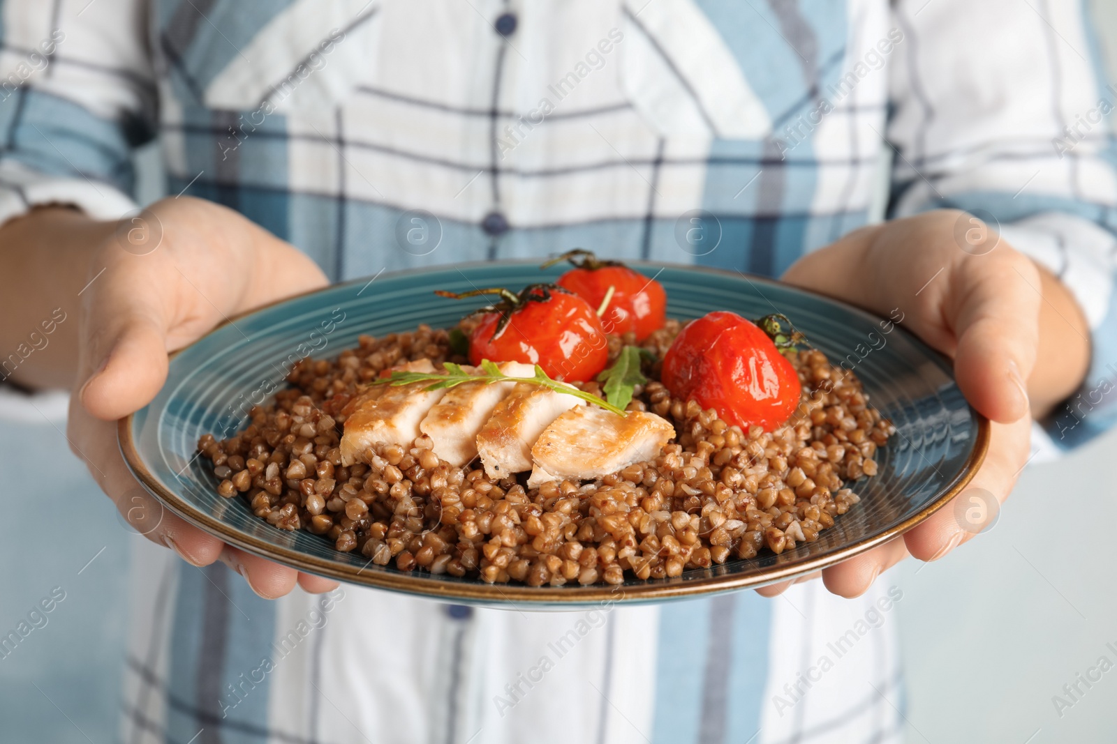 Photo of Woman holding plate of buckwheat porridge with meat and tomatoes, closeup