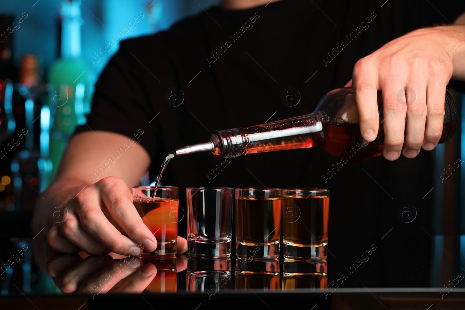 Photo of Bartender pouring alcohol drink into shot glass at mirror counter in bar, closeup