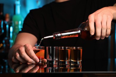 Bartender pouring alcohol drink into shot glass at mirror counter in bar, closeup