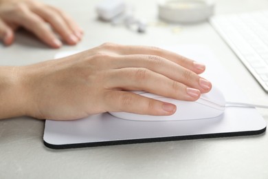 Photo of Woman using wired computer mouse on pad at light grey marble table, closeup
