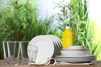 Set of clean dishware and detergent on white table against blurred background