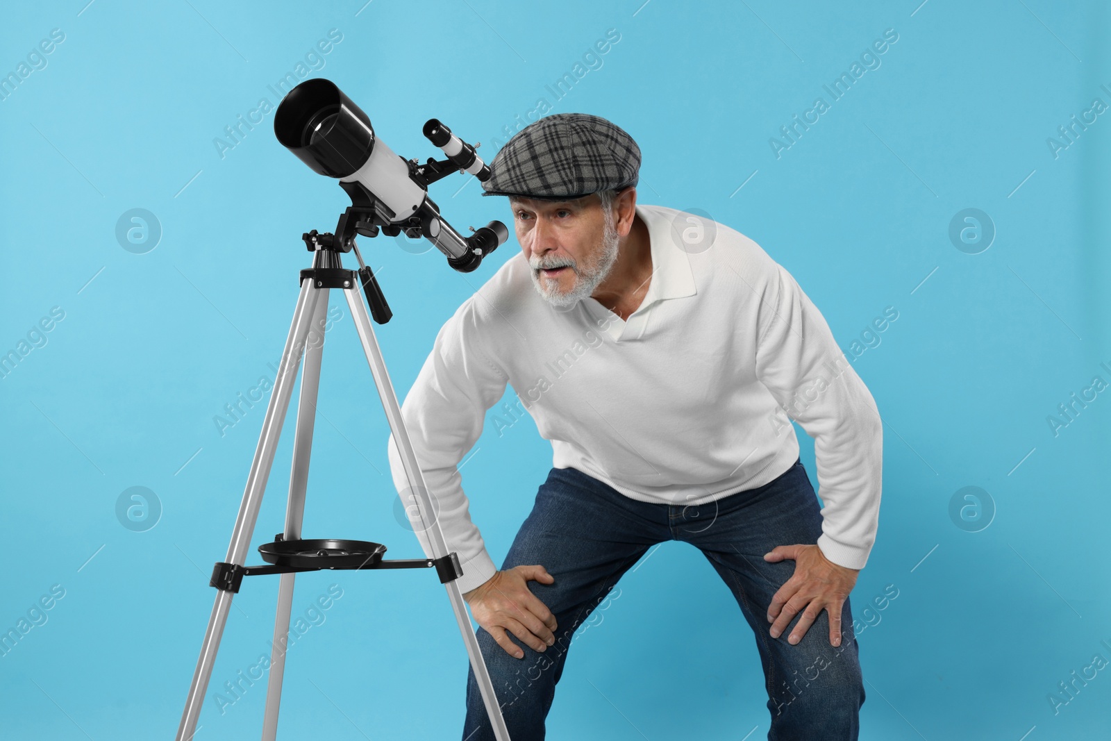 Photo of Senior astronomer looking at stars through telescope on light blue background