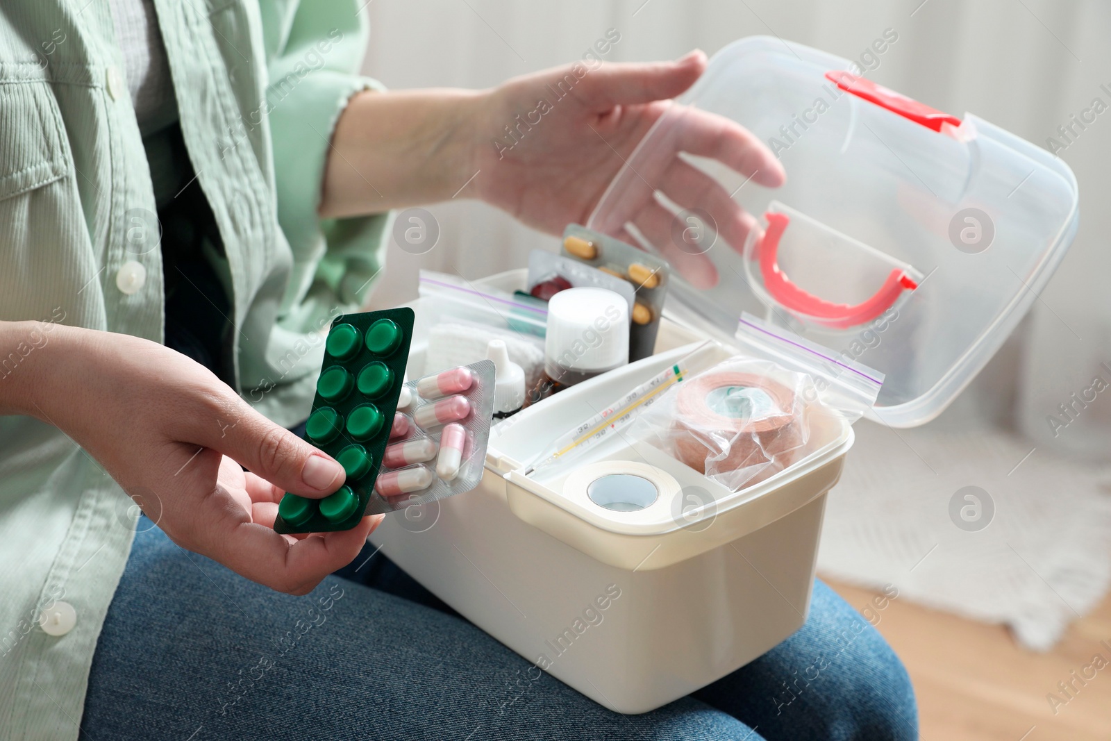 Photo of Woman putting pills into first aid kit indoors, closeup