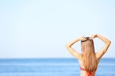 Young woman in red bikini near sea. Space for text