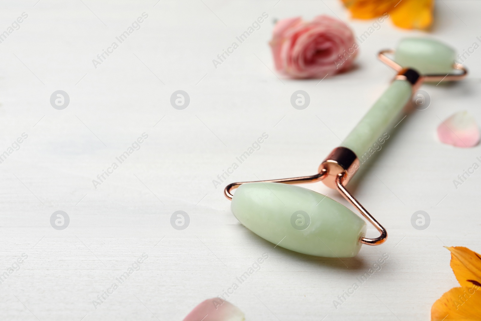 Photo of Natural jade face roller and flowers on white wooden background. Space for text