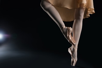 Photo of Ballerina in pointe shoes dancing on black background, closeup. Space for text