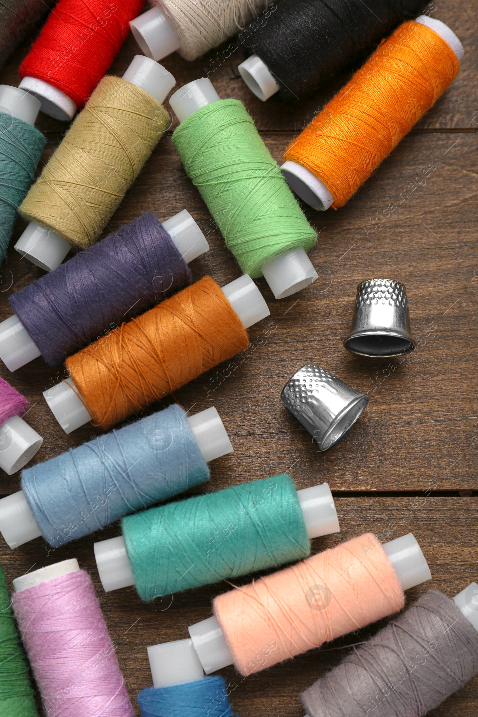 Photo of Colorful threads and sewing thimbles on wooden table, flat lay