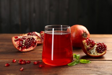 Photo of Tasty pomegranate juice in glass and fresh fruits on wooden table