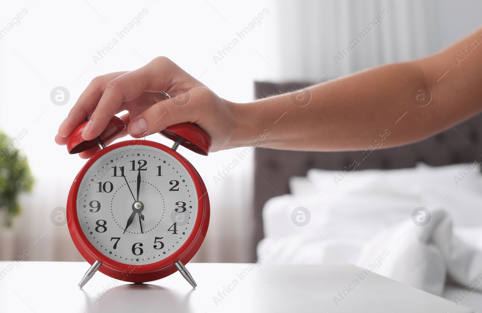 Photo of Woman turning off alarm clock on table in bedroom. Time to wake up