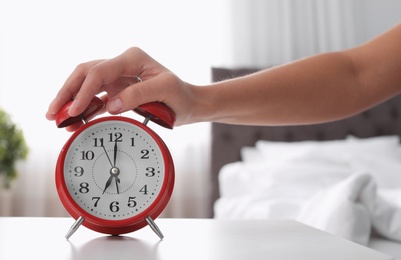 Woman turning off alarm clock on table in bedroom. Time to wake up