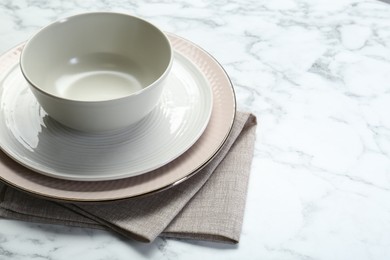 Clean plates, bowl and napkin on white marble table, closeup. Space for text