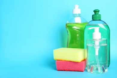 Detergents and sponges on light blue background, space for text. Clean dishes