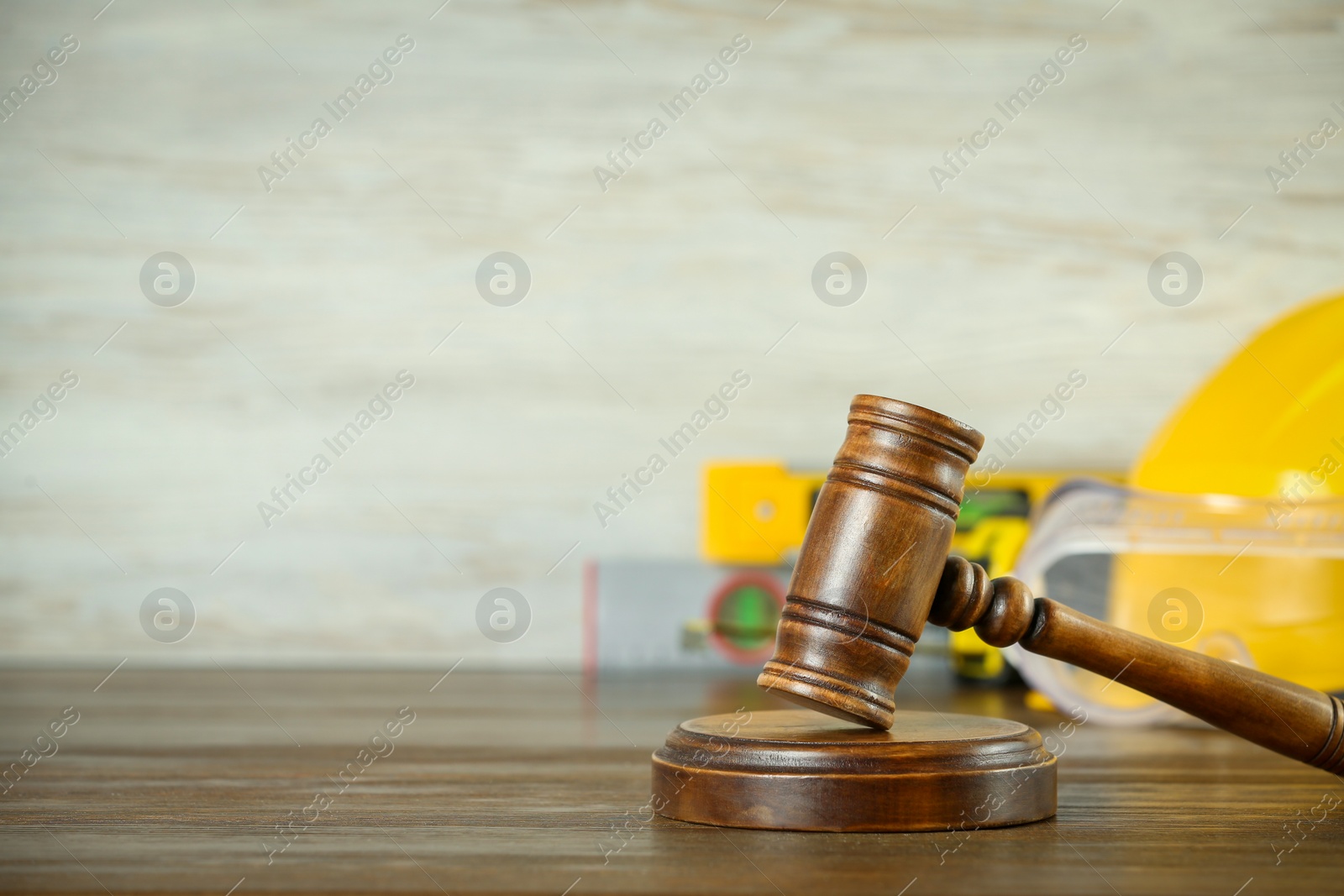 Photo of Construction and land law concepts. Judge gavel, helmet, safety glasses with level on wooden table, space for text