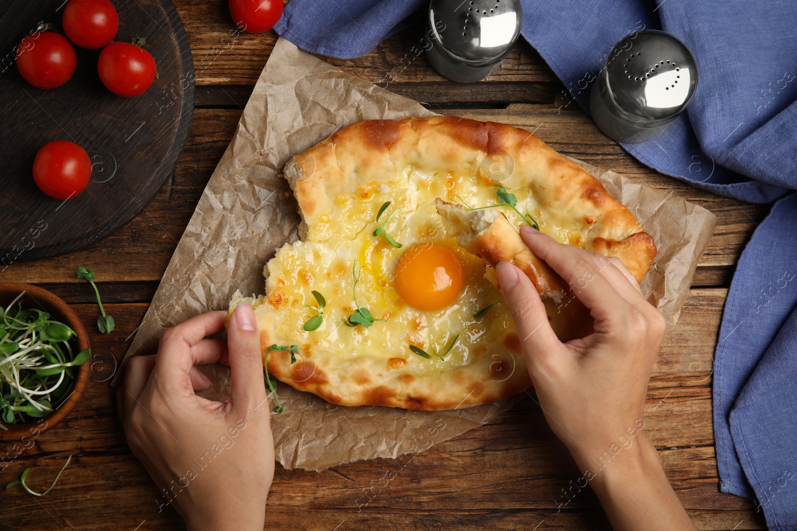 Photo of Top view of woman eating delicious Adjarian khachapuri at wooden table, closeup