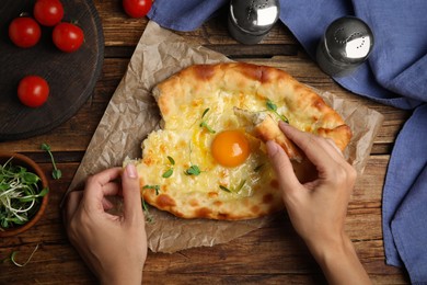 Top view of woman eating delicious Adjarian khachapuri at wooden table, closeup