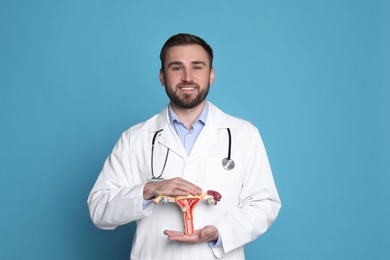 Photo of Doctor demonstrating model of female reproductive system on light blue background. Gynecological care
