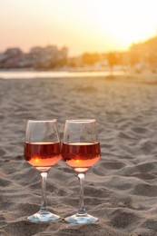 Photo of Glasses of tasty rose wine on sandy beach, space for text