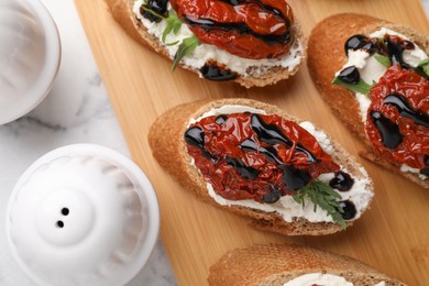 Photo of Delicious bruschettas with sun-dried tomatoes, cream cheese and balsamic vinegar on white table, flat lay