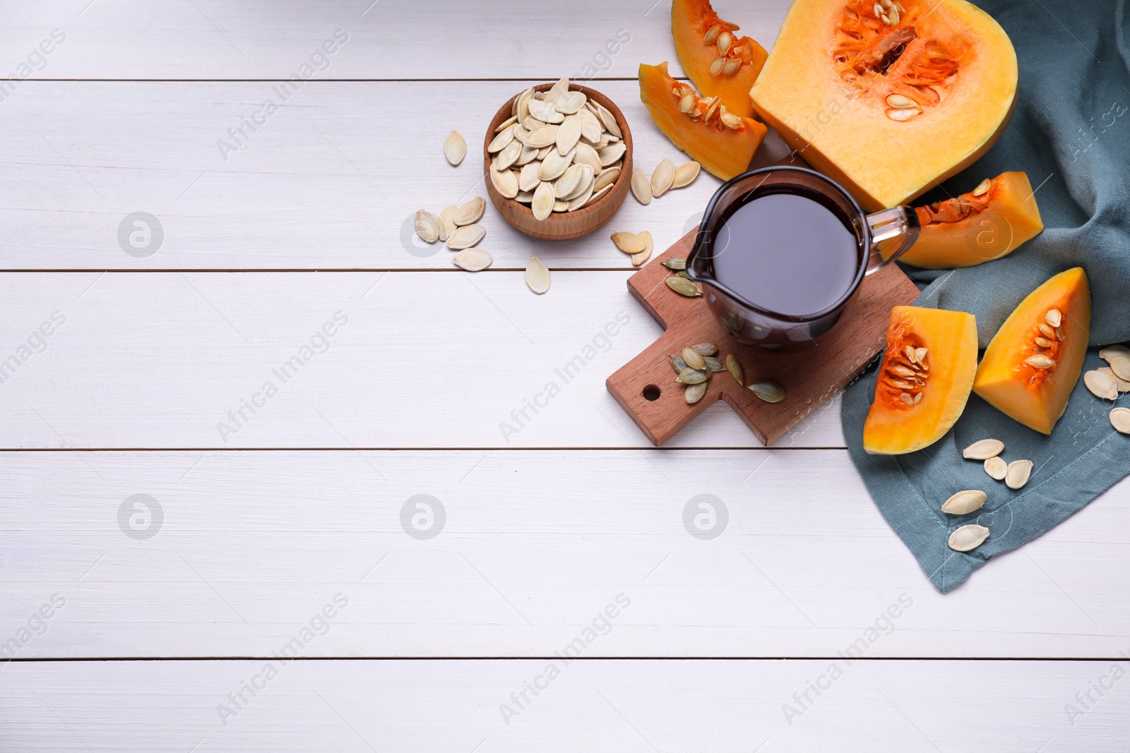 Photo of Flat lay composition with pumpkin seed oil in glass pitcher on white wooden table. Space for text