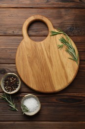 Photo of Cutting board, salt, pepper and rosemary on wooden table, flat lay. Space for text