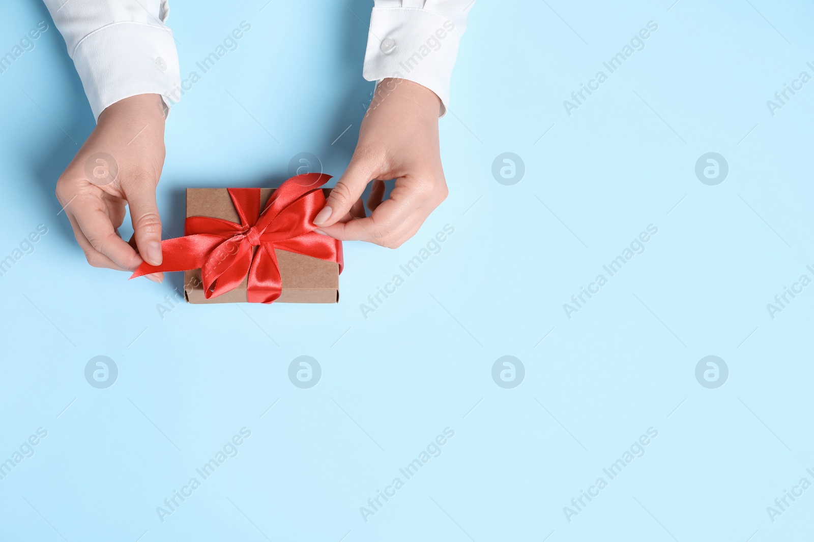 Photo of Woman with gift box on light blue background, top view. Space for text