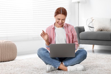 Woman waving hello during video chat via laptop at home