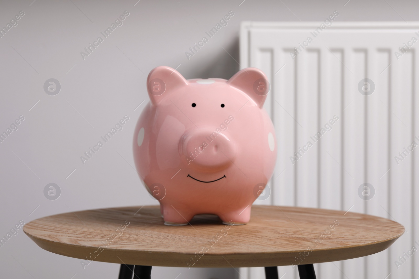 Photo of Piggy bank on wooden table near heating radiator