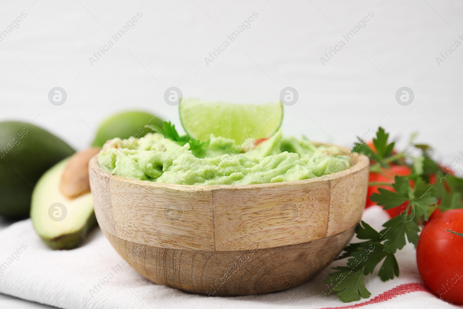 Photo of Bowl of delicious guacamole and ingredients on white table, closeup