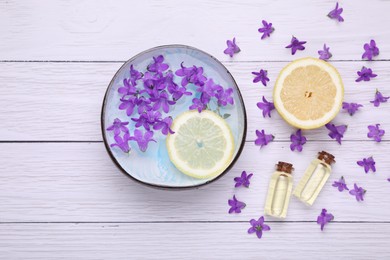 Bowl with water, lemon, purple flowers and bottles of essential oils on white wooden table, flat lay. Spa composition