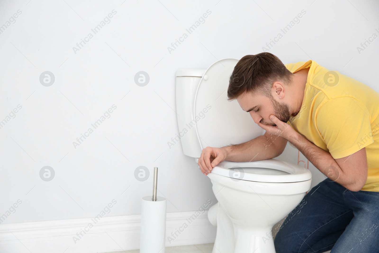 Photo of Young man suffering from nausea over toilet bowl indoors