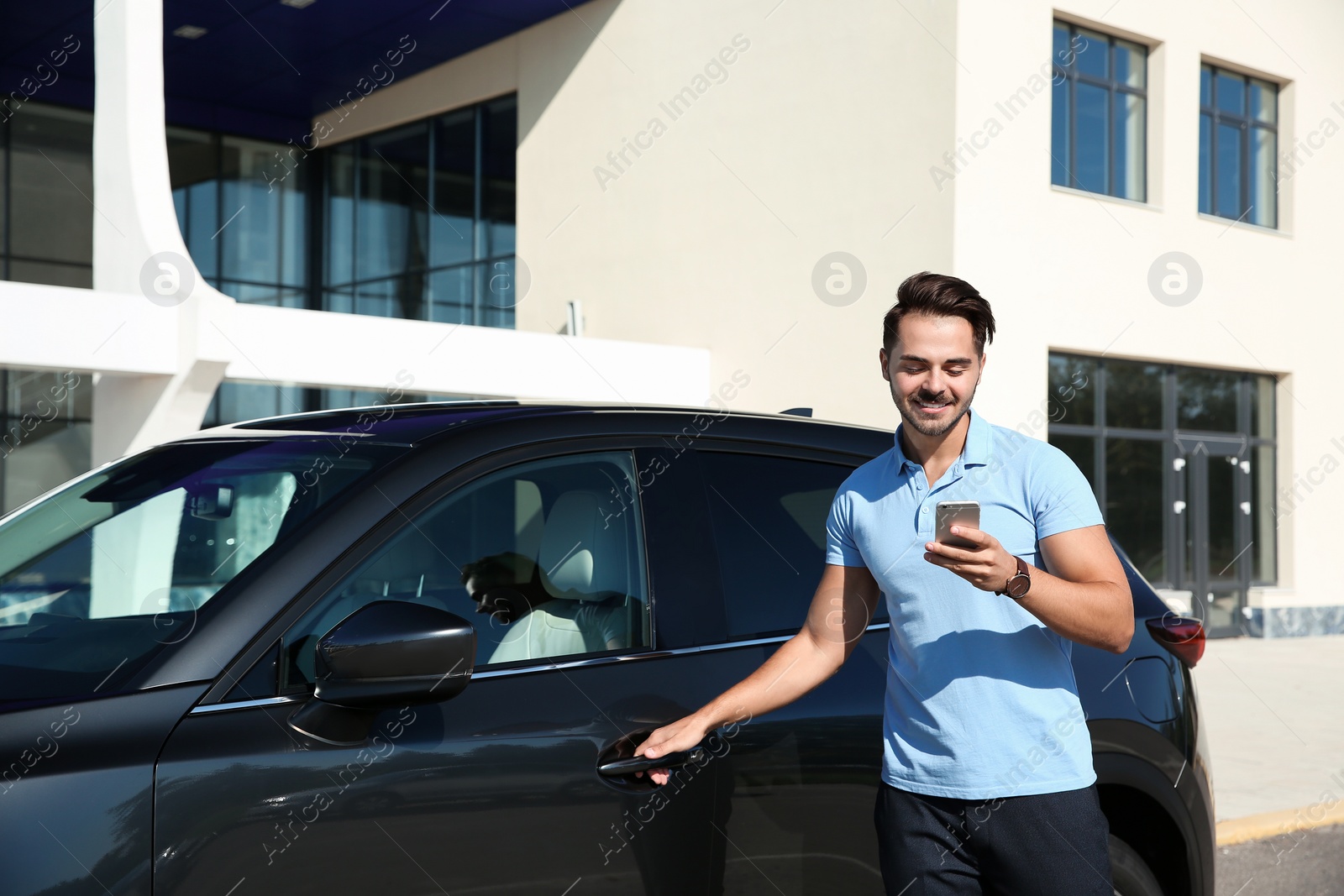 Photo of Young man using phone near modern car, outdoors