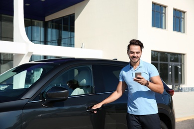 Photo of Young man using phone near modern car, outdoors
