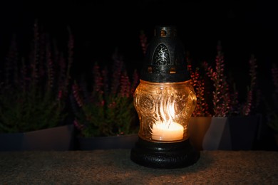 Photo of Grave lantern with burning candle on stone surface at night, space for text