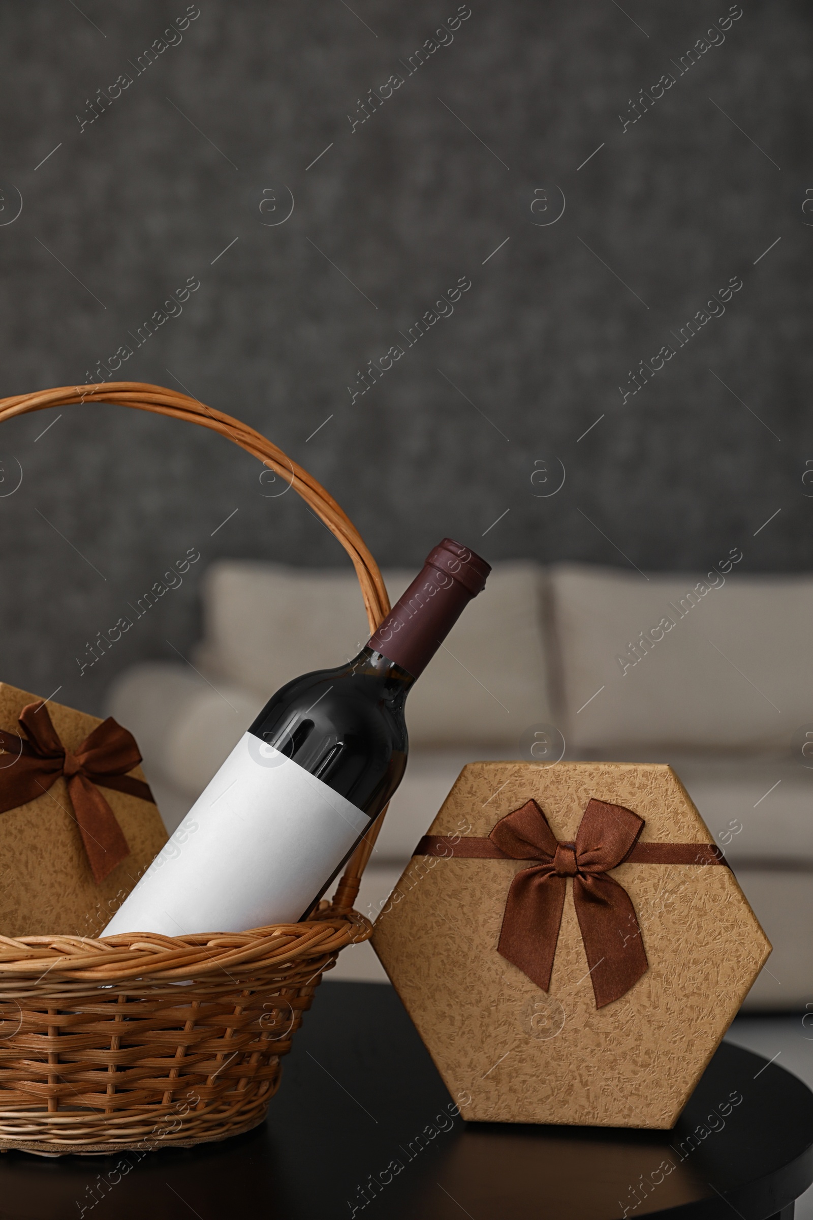 Photo of Wicker basket with bottle of wine and gift boxes on table in room. Space for design