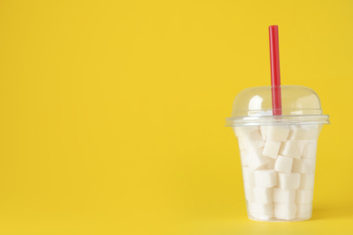 Photo of Refined sugar cubes in plastic cup with straw on yellow background. Space for text