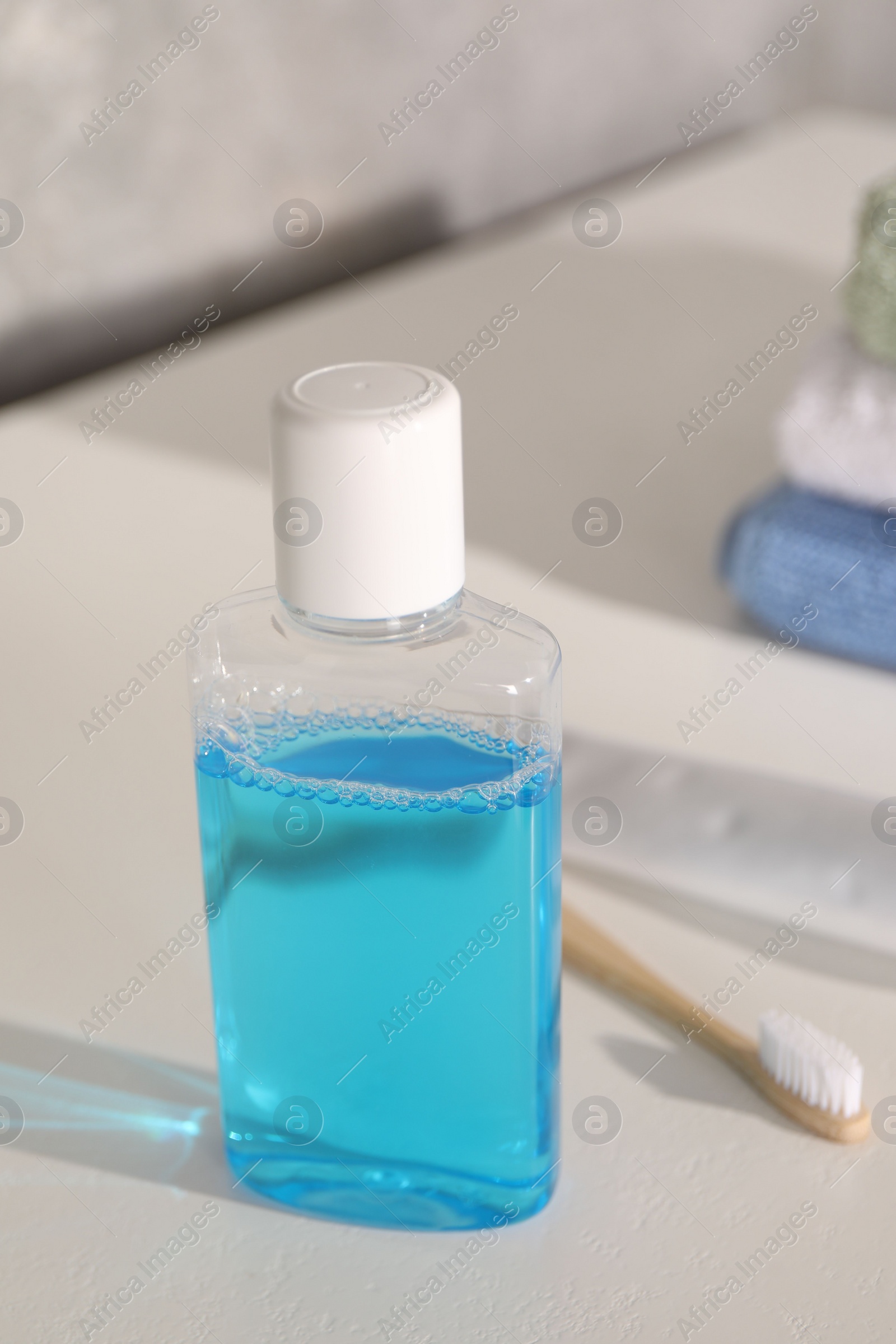 Photo of Bottle of mouthwash and toothbrush on white table in bathroom