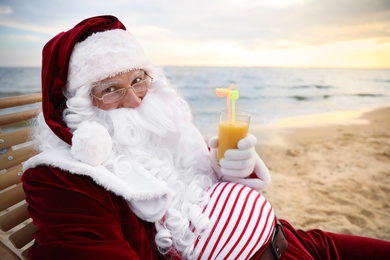 Photo of Santa Claus with cocktail relaxing on beach. Christmas vacation