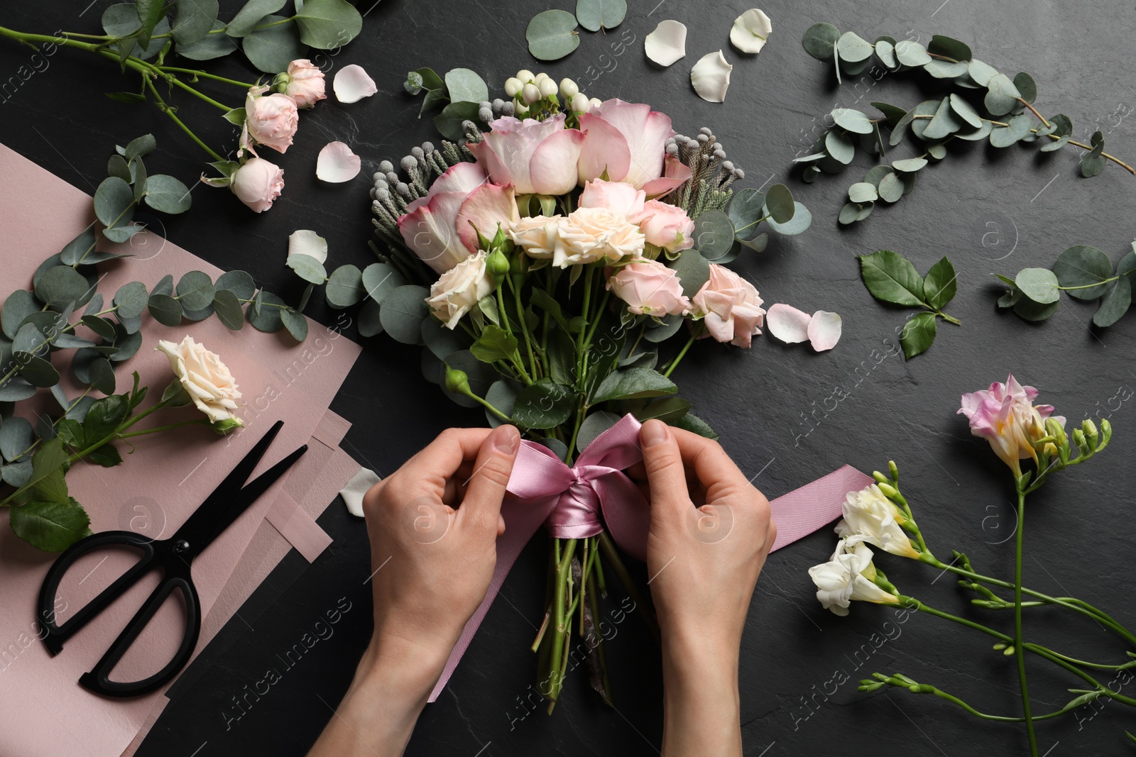 Photo of Florist creating beautiful bouquet at black table, top view