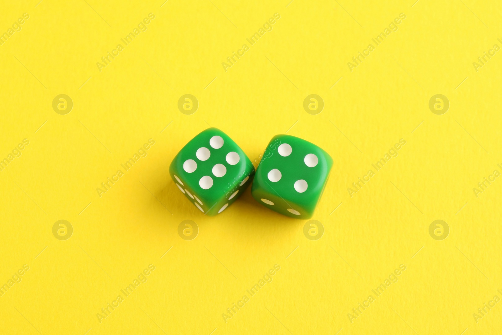 Photo of Two green game dices on yellow background, top view. Space for text