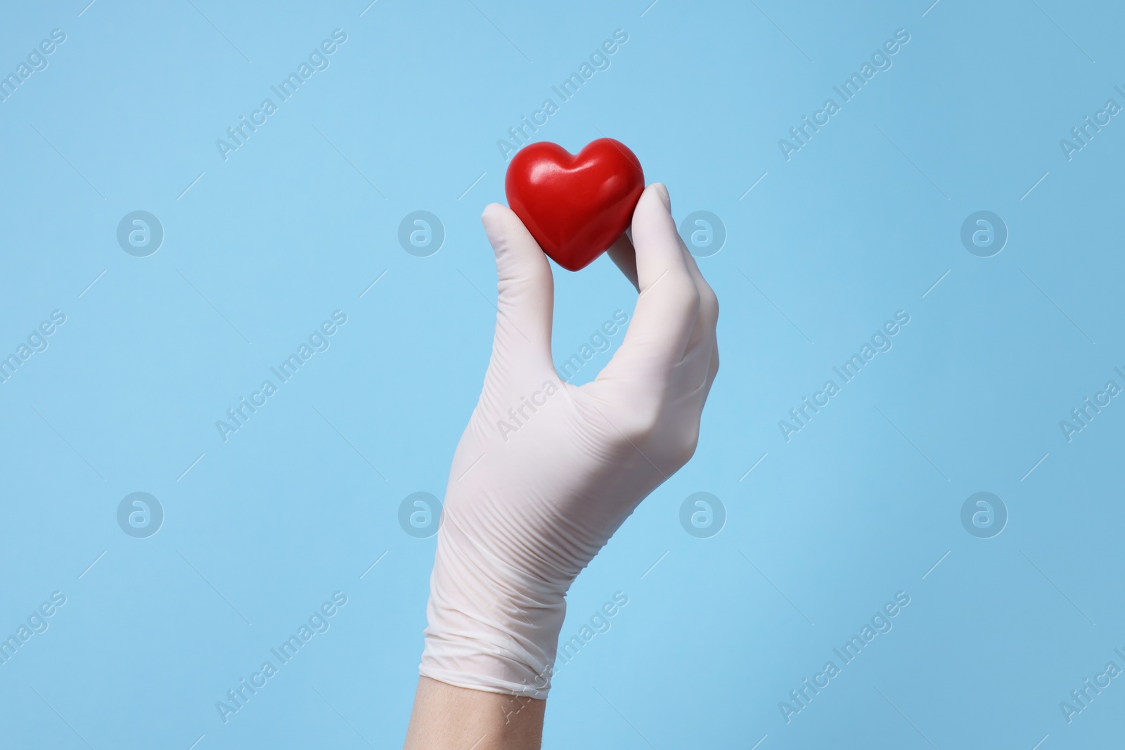 Photo of Doctor wearing white medical glove holding decorative heart on light blue background, closeup