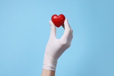 Photo of Doctor wearing white medical glove holding decorative heart on light blue background, closeup