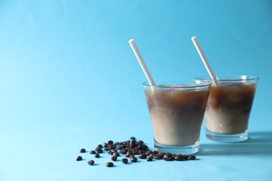 Photo of Refreshing iced coffee with milk in glasses and beans on light blue background. Space for text