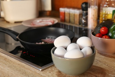 Many fresh eggs on wooden countertop in kitchen. Frying bacon for breakfast