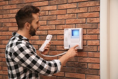 Man pressing button on intercom panel indoors