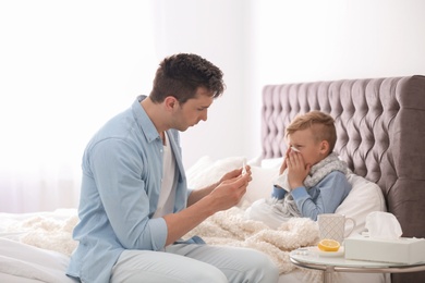 Photo of Father taking care of little son suffering from cold in bed