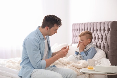 Father taking care of little son suffering from cold in bed