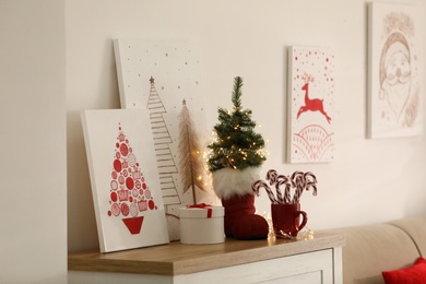 Photo of Beautiful Christmas pictures on chest of drawers indoors. Interior design